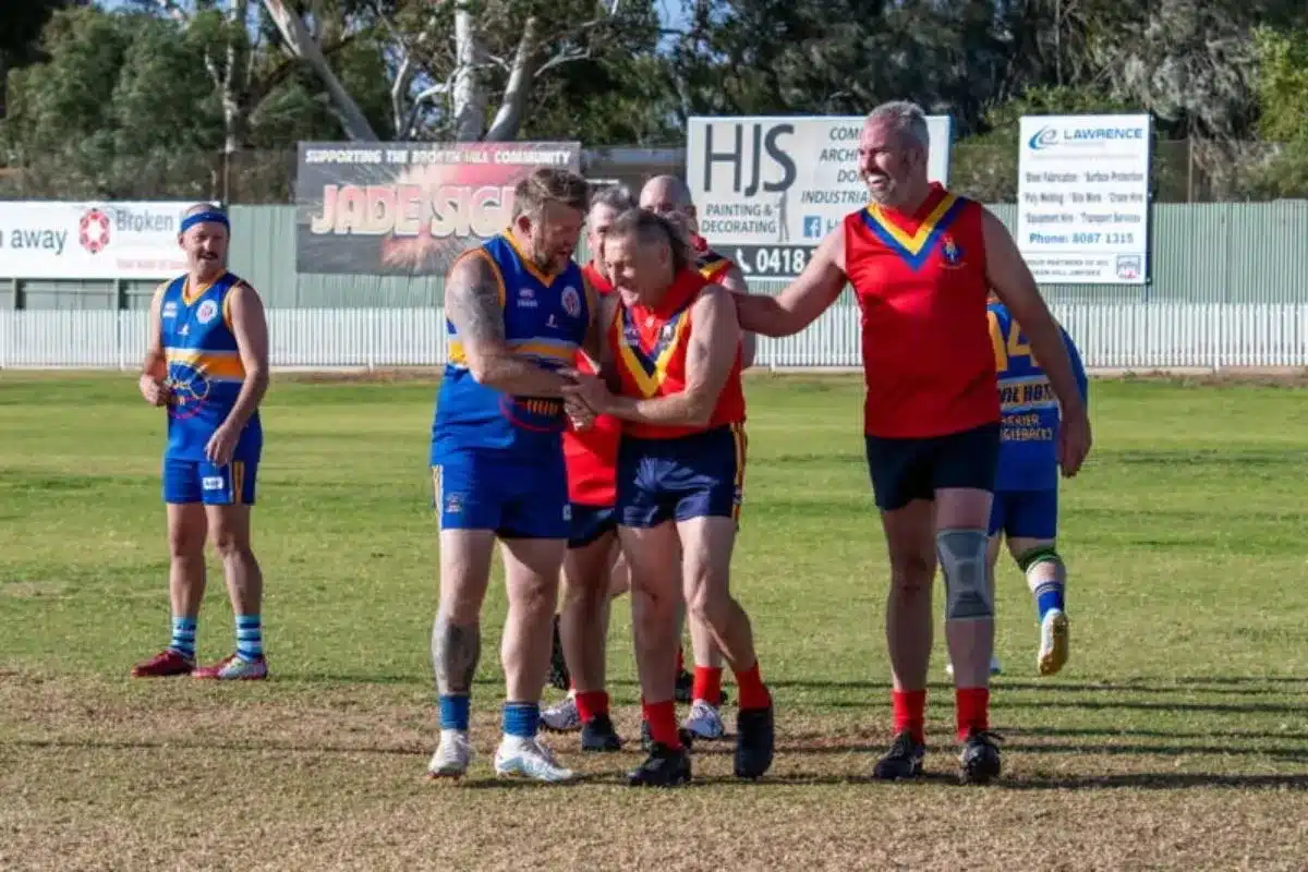 Robbie Johnstone is congratulated by teammates and opponents after the match - players in red and blue guernseys embracing on the field