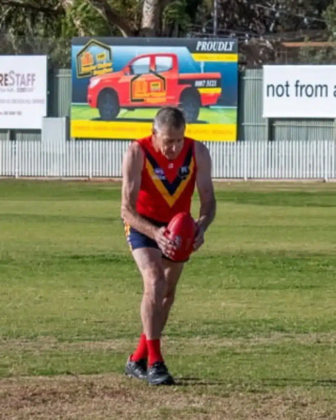 player in red and gold guernsey kicking the ball on the boundary