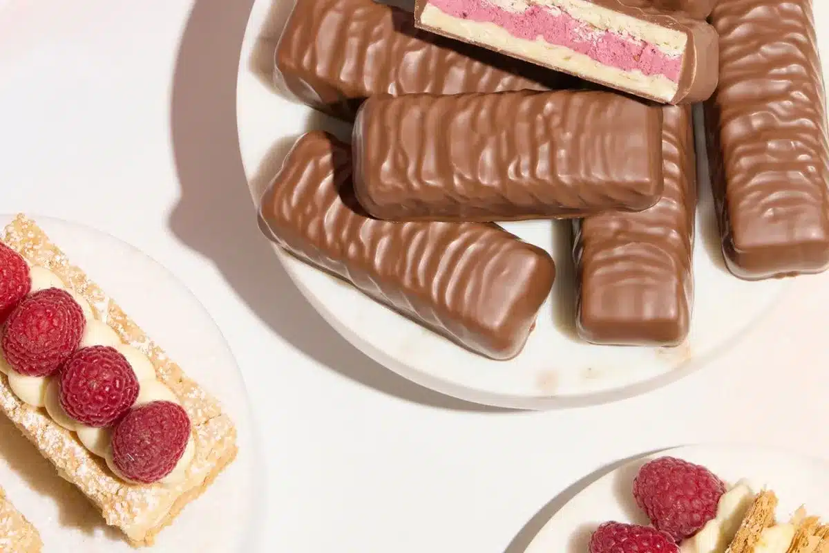 Milk Raspberry Mille Feuille Bars piled on a marble plate, with one cut open to show the layered interior, alongside fresh raspberry mille feuille pastries