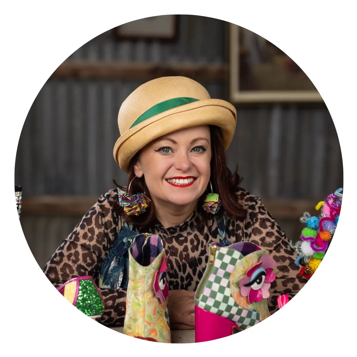 Katie Spain, wearing a straw hat and leopard print top, smiling beside colourful decorative boots.