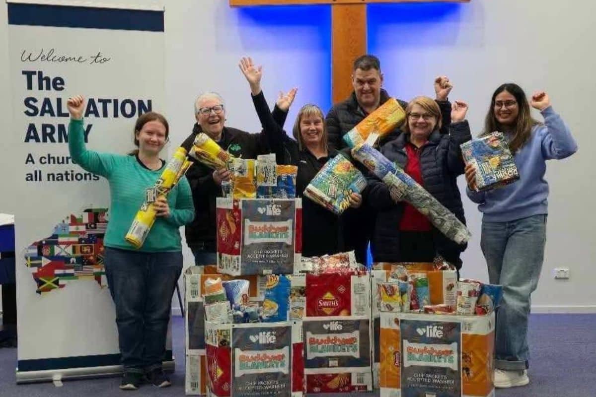 Life FM and Salvation Army volunteers celebrate the handover of 80 Buddy Blankets - group celebrating with rolled blankets in front of The Salvation Army banner