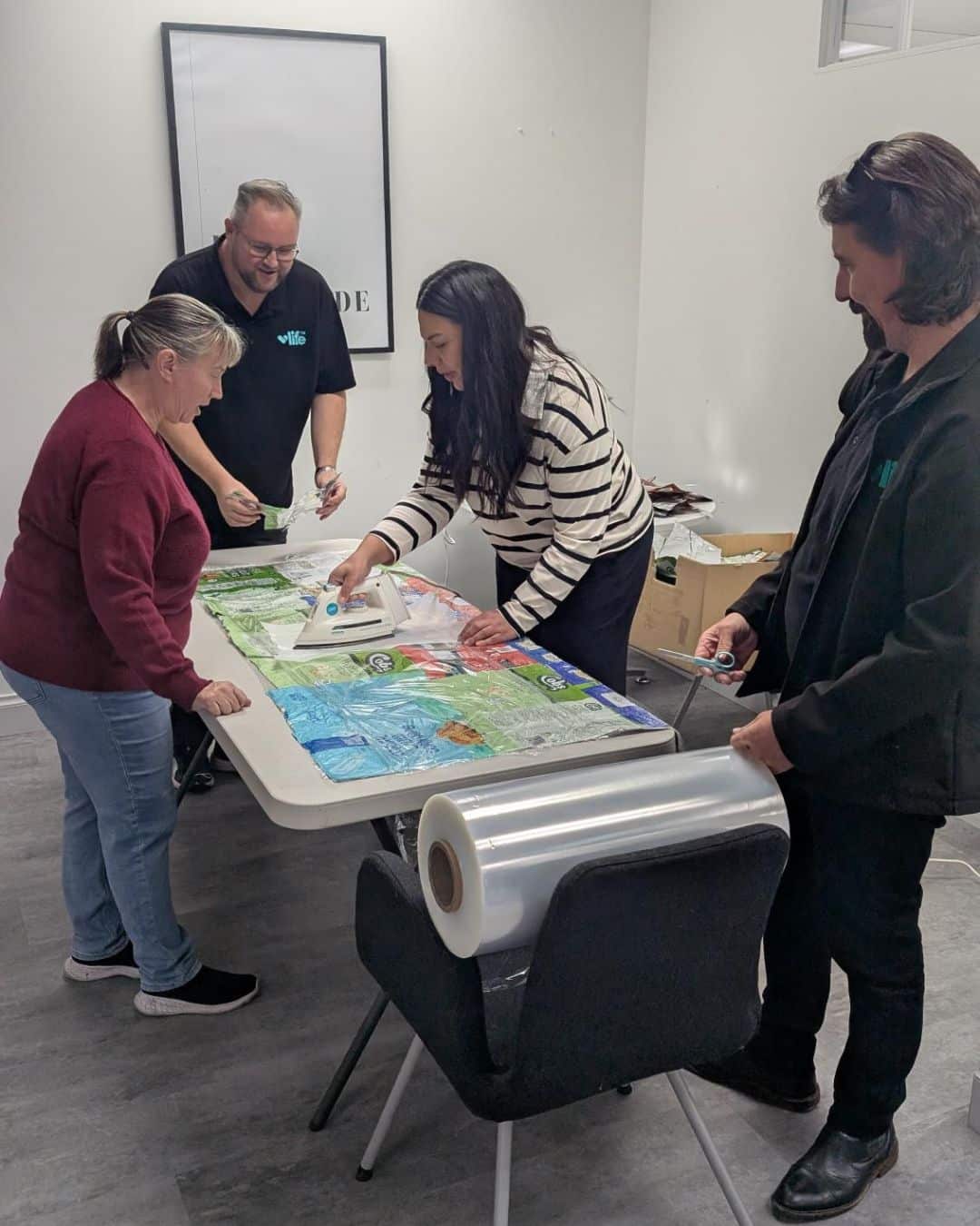 Volunteers press and seal chip packets together to form a Buddy Blanket - four volunteers working together to iron and laminate a blanket made of chip packets