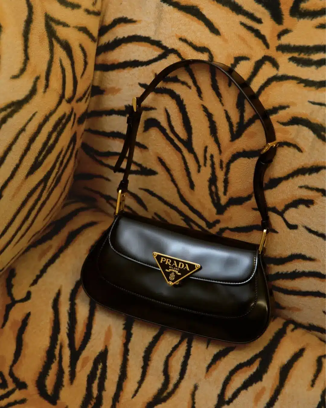Black leather Prada shoulder bag with gold triangle logo resting on a tiger print fabric background.