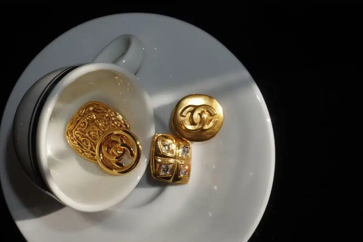 Vintage Chanel gold jewellery including a ring, brooch and earrings displayed on a white teacup and saucer.