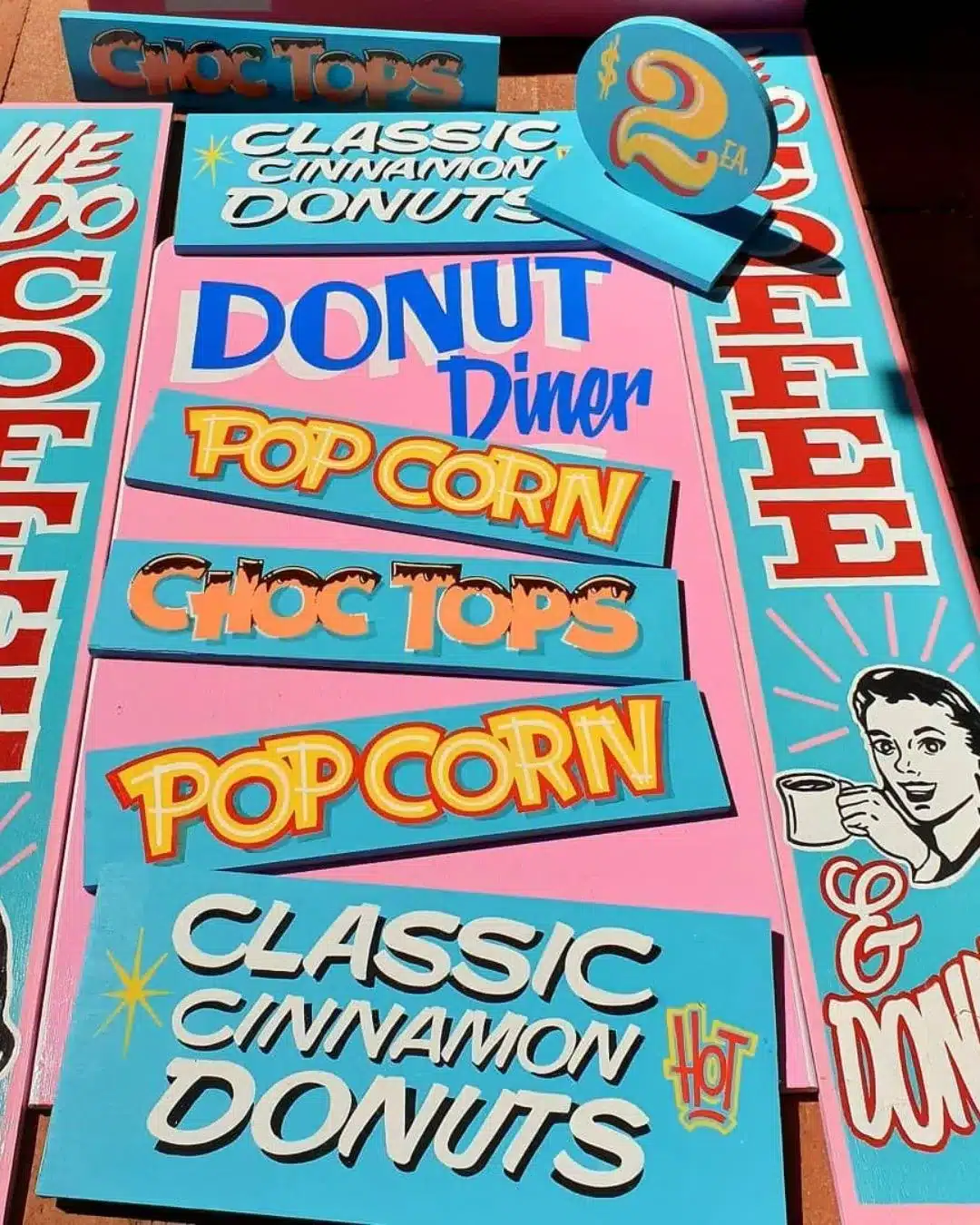 Hand-painted retro style signage reading donuts, coffee and pop corn in bright pink and blue lettering.