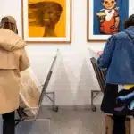 Two gallery visitors examine framed Polish posters on the wall at Galeria Grafika.