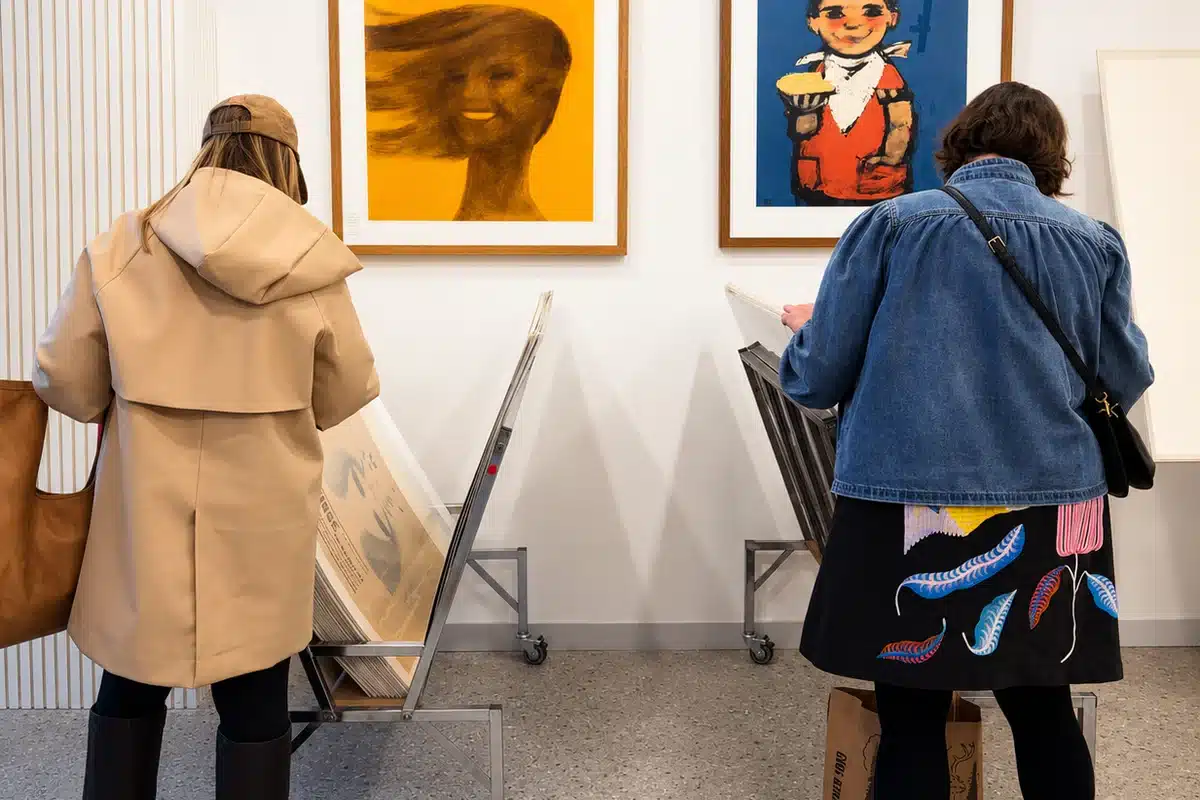 Two gallery visitors examine framed Polish posters on the wall at Galeria Grafika.
