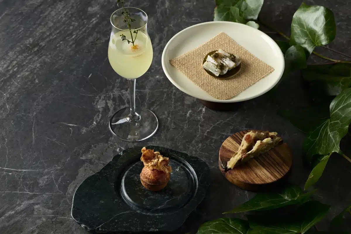 Hardy's Verandah - mocktail garnished with herb sprig, served alongside Chicken Millefeuille, Kelp Taco and Artichoke Pop dishes.