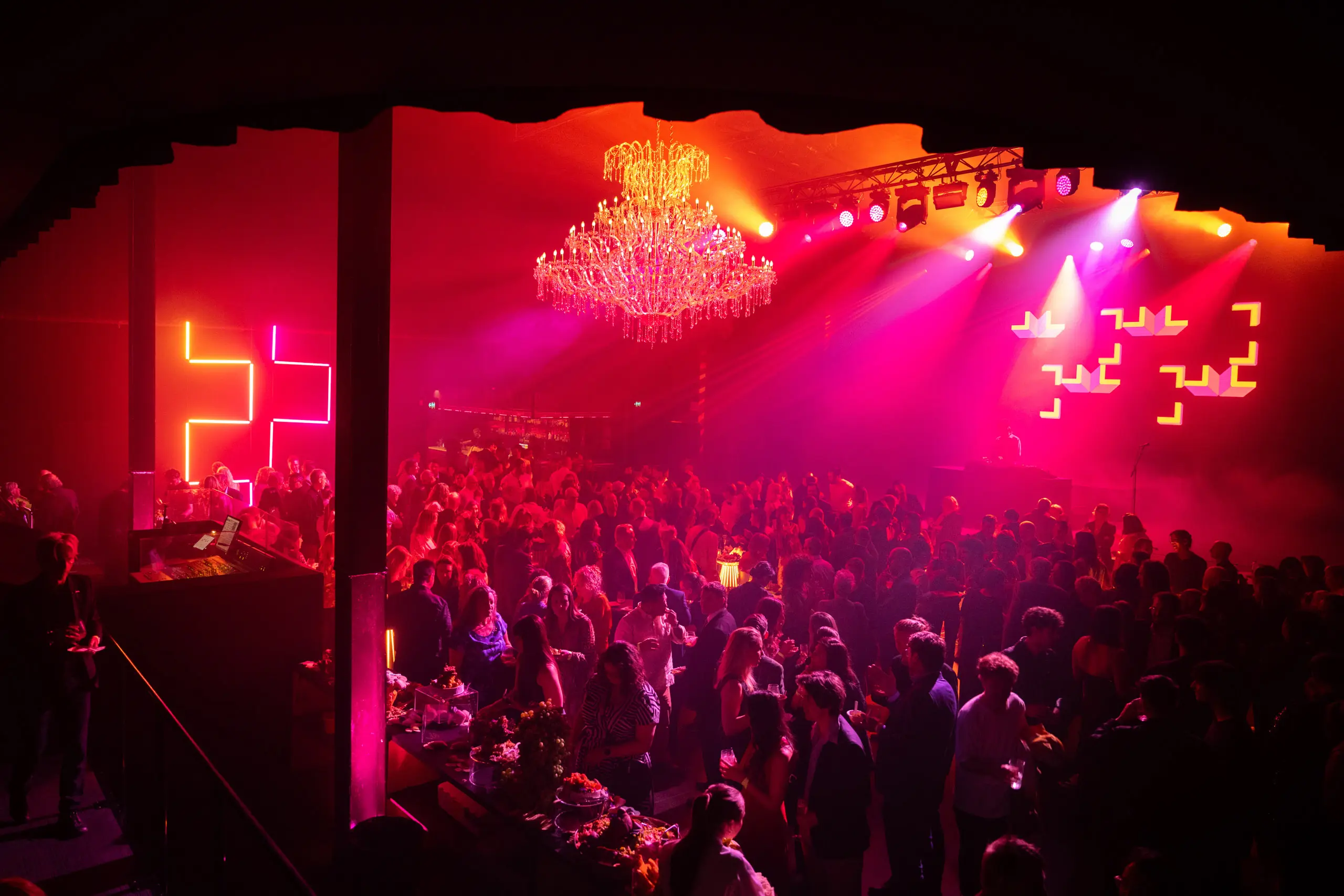 Audience enjoying a live performance or festival event under colourful stage lighting.