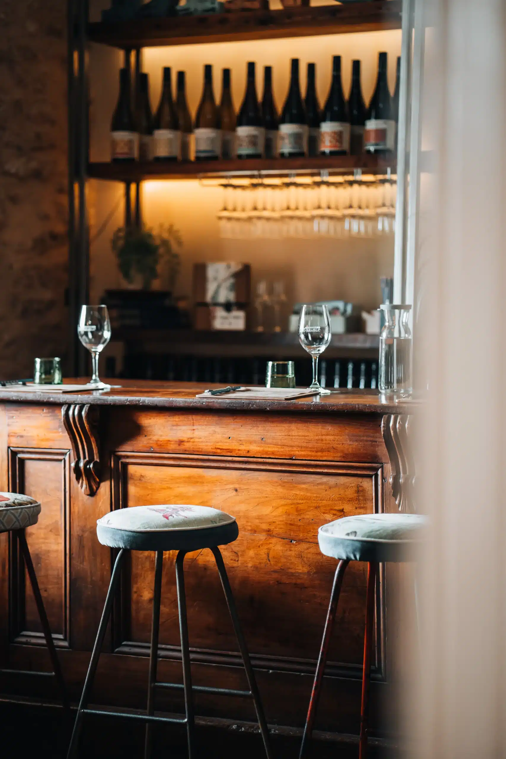 Timber cellar door bar with wine glasses, a water carafe and shelves of Lino Ramble bottles in the background.